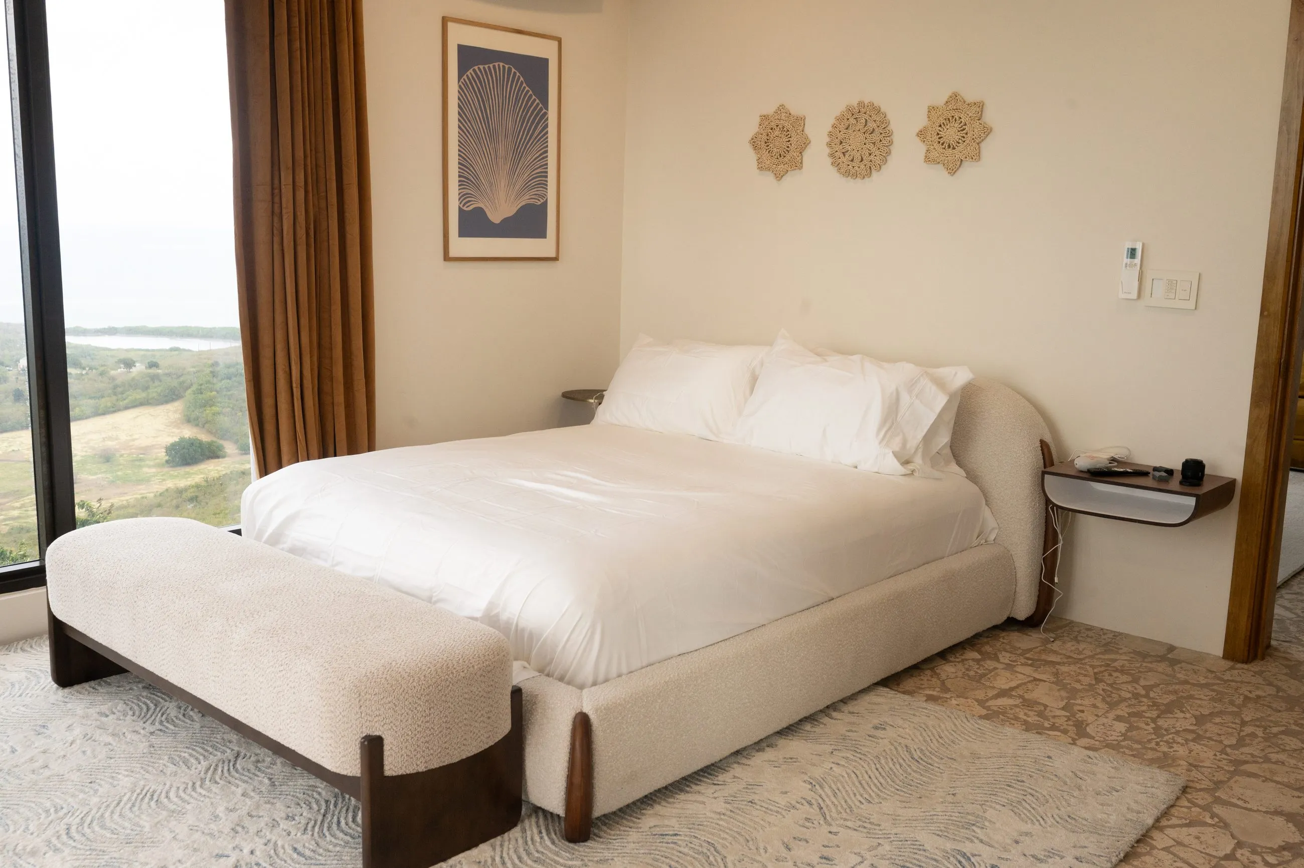 Second bedroom with a wide window wall over the hills and ocean, upholstered king bed and woven wall discs
