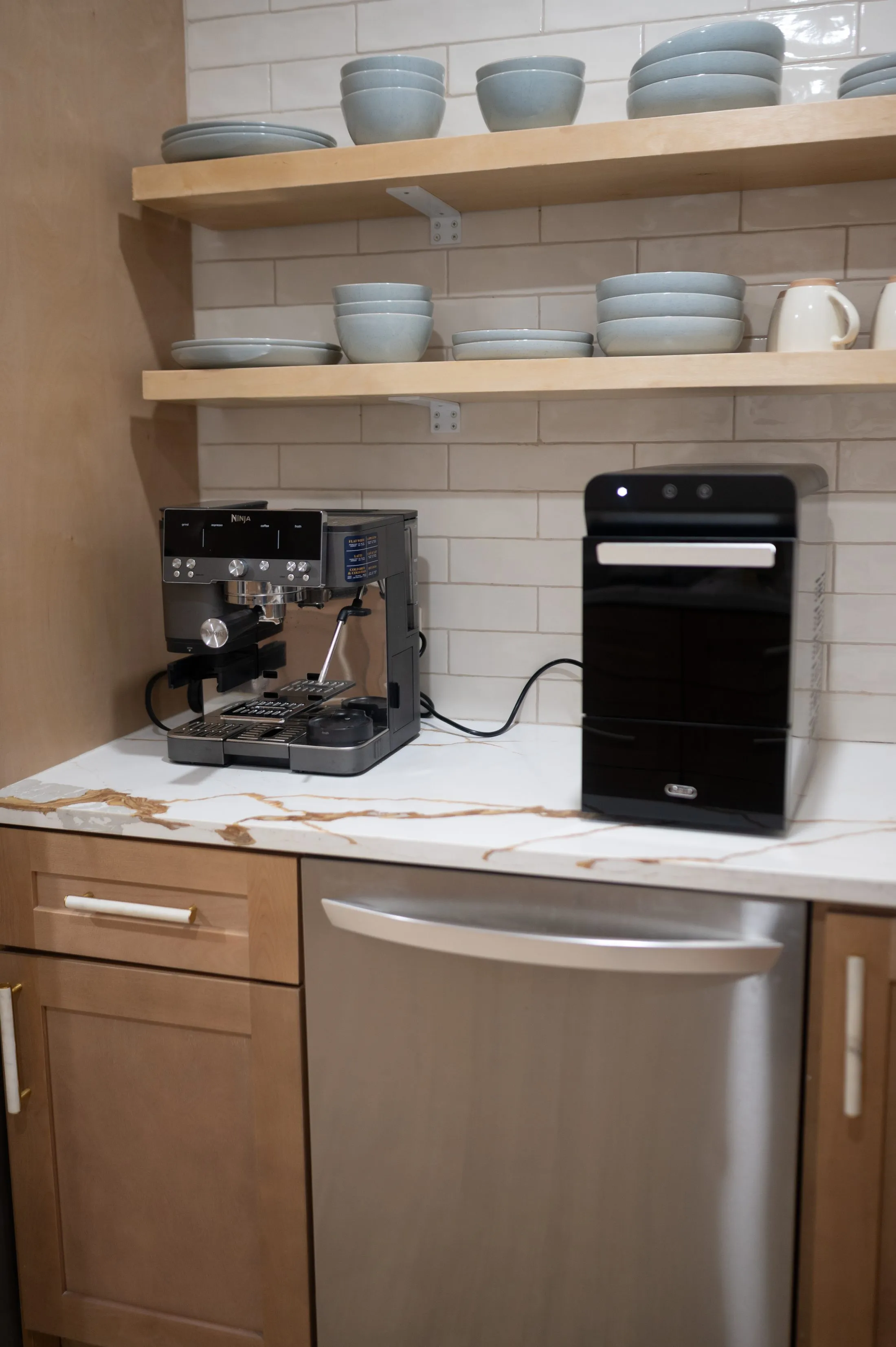 Kitchen counter with an espresso machine, open wood shelving stacked with crockery and a marble worktop