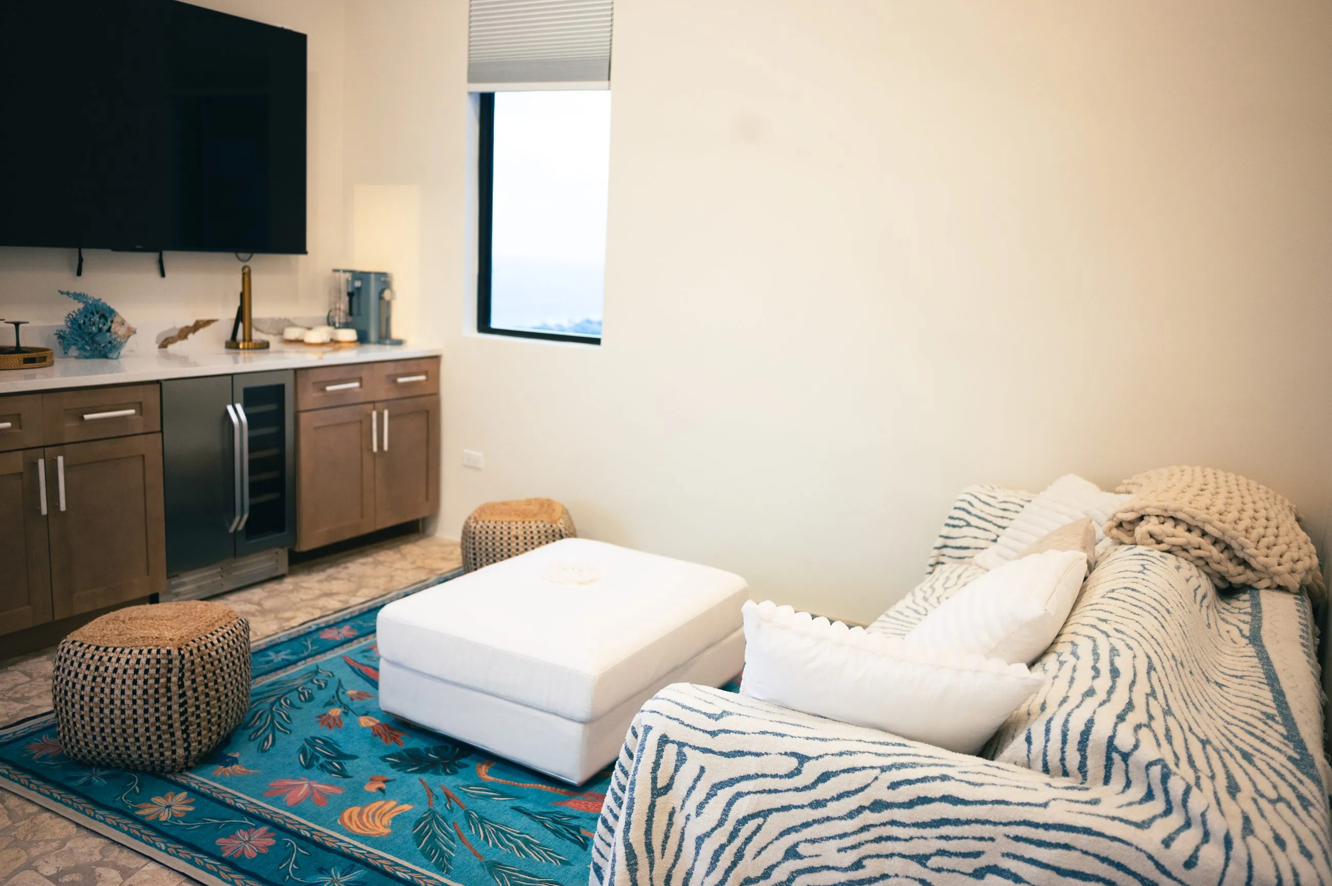 Living room with a wall-mounted television, wet bar, turquoise patterned rug and a sofa that converts to a queen bed