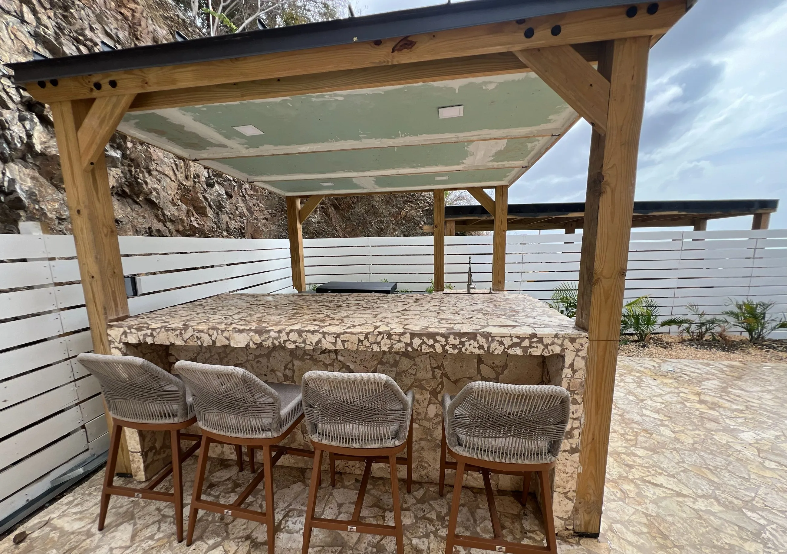 Covered outdoor bar with a stone counter, four stools and a timber pergola on the pool deck