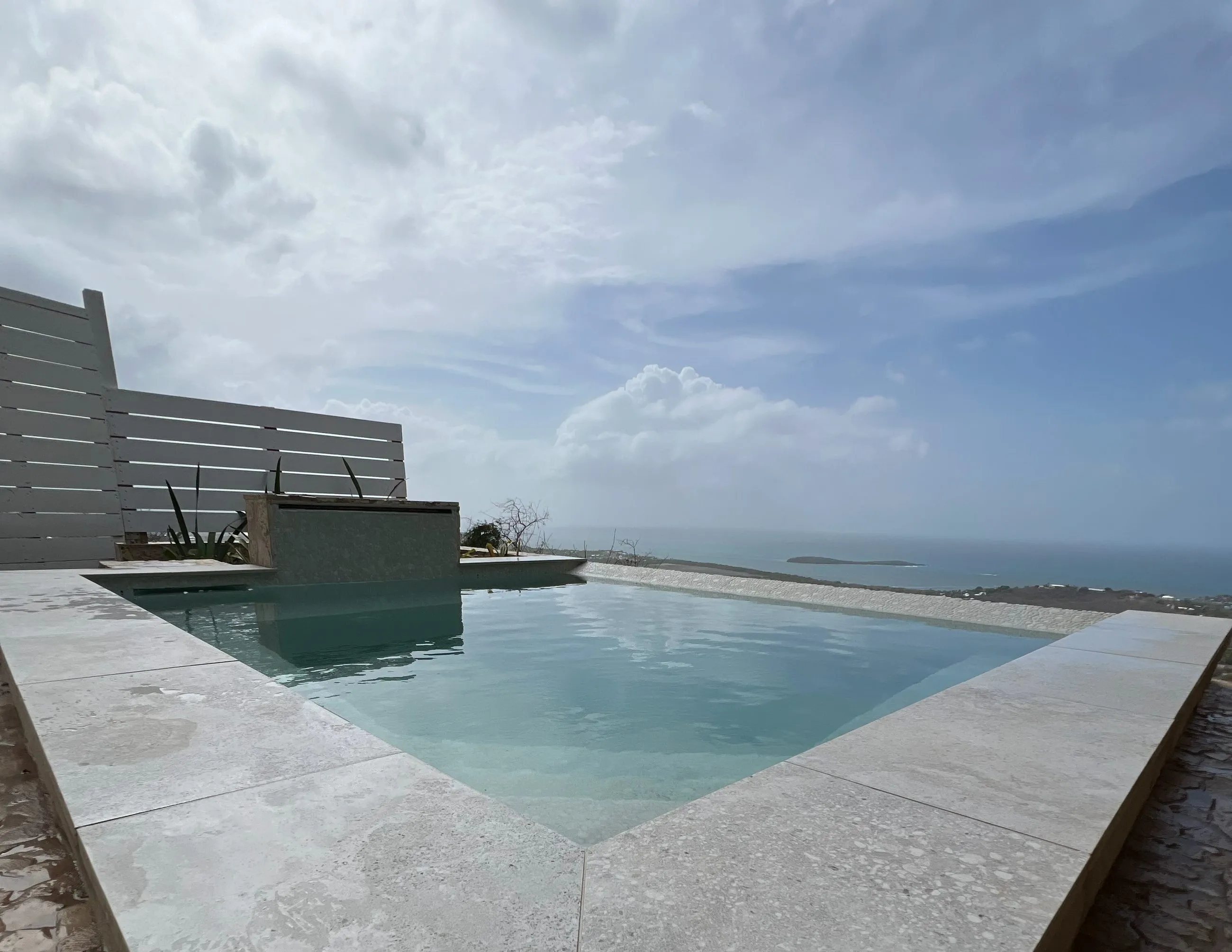 The soaking pool with its infinity edge running out towards the open Caribbean, travertine coping and a spillover water feature